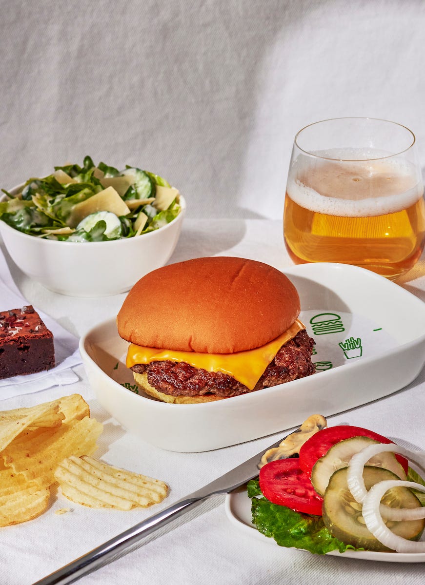 Delta Air Lines, Shake Shack, burgers, first class, in-flight meals, Atlanta, Los Angeles, New York-LaGuardia, Seattle, cheeseburger, Angus beef, potato bun, ShackSauce, Caesar salad, brownie, airline partnership, travel, food, onboard service, Stephanie Laster, Michael Kark, Natalie Neysa Alund
